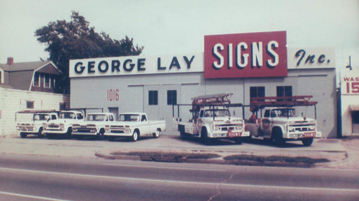 This 1965 photo shows the original George Lay Signs building on the left and a 1963 addition to its right. To the south of that building, a longtime laundromat’s 15-cent wash sign is barely visible. George Lay Signs recently purchased and razed that building. To the north of the company’s building is a slim building where a barbershop once was. The company bought that building and the 2-story house next to it in about 1973. It demolished the buildings and expanded its building to the north.