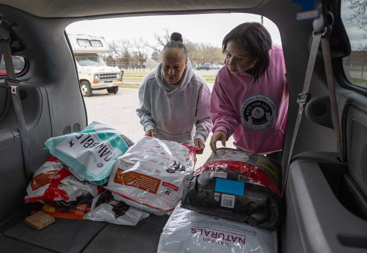 Maria Montoya, left, and Kylee Wallentine grab dog food from the back of a van to give to a family in Planeview.