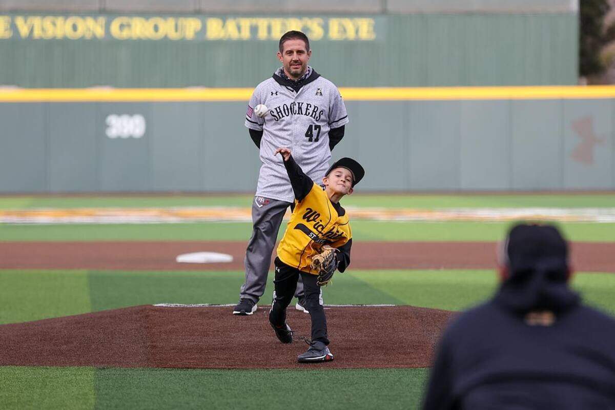 Michael Church (background) watches his 8-year-old son, Kendric, throw out the first pitch at a Wichita State baseball game in March. Michael was diagnosed with a terminal brain cancer in February.