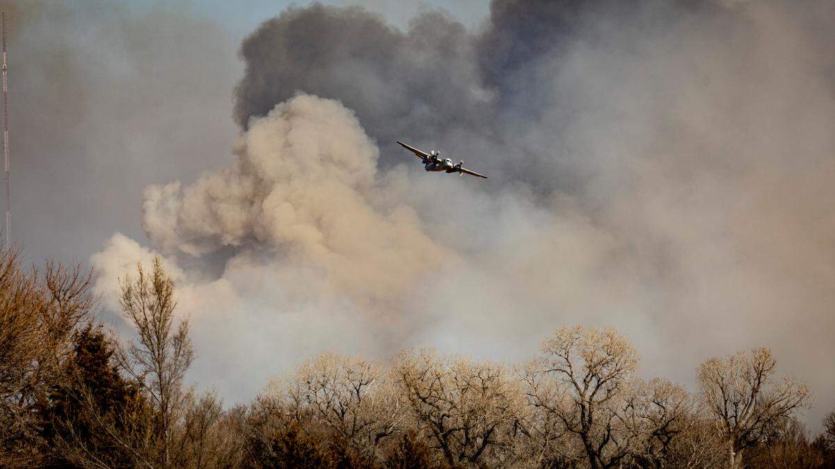 A tanker plane flies away from a large wildfire in Reno County after dropping its load of water on the fire Saturday afternoon. Officials confirmed Sunday that one person has died in the fire.