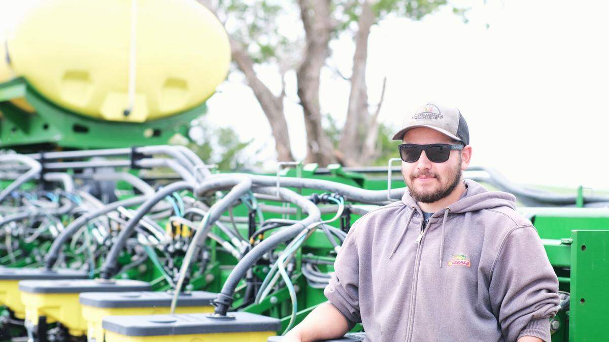 Alex Millershaski stands next to a seed planter used for crops like wheat, corn and sorghum.