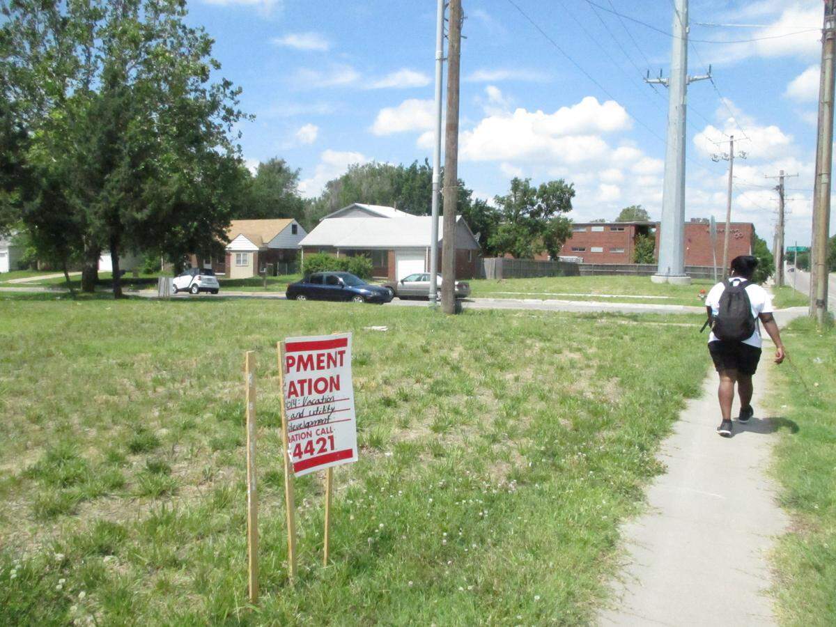 A torn sign marks the site of a parking lot for two new apartment buildings. The houses in the background will be torn down.