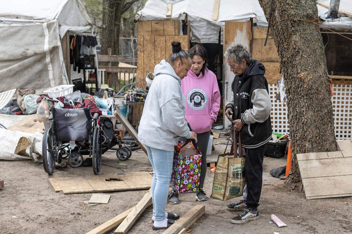 Maria Montoya, left, and Kylee Wallentine, middle, deliver food and pet items to Anna Robinson at her homeless encampment in Planeview.