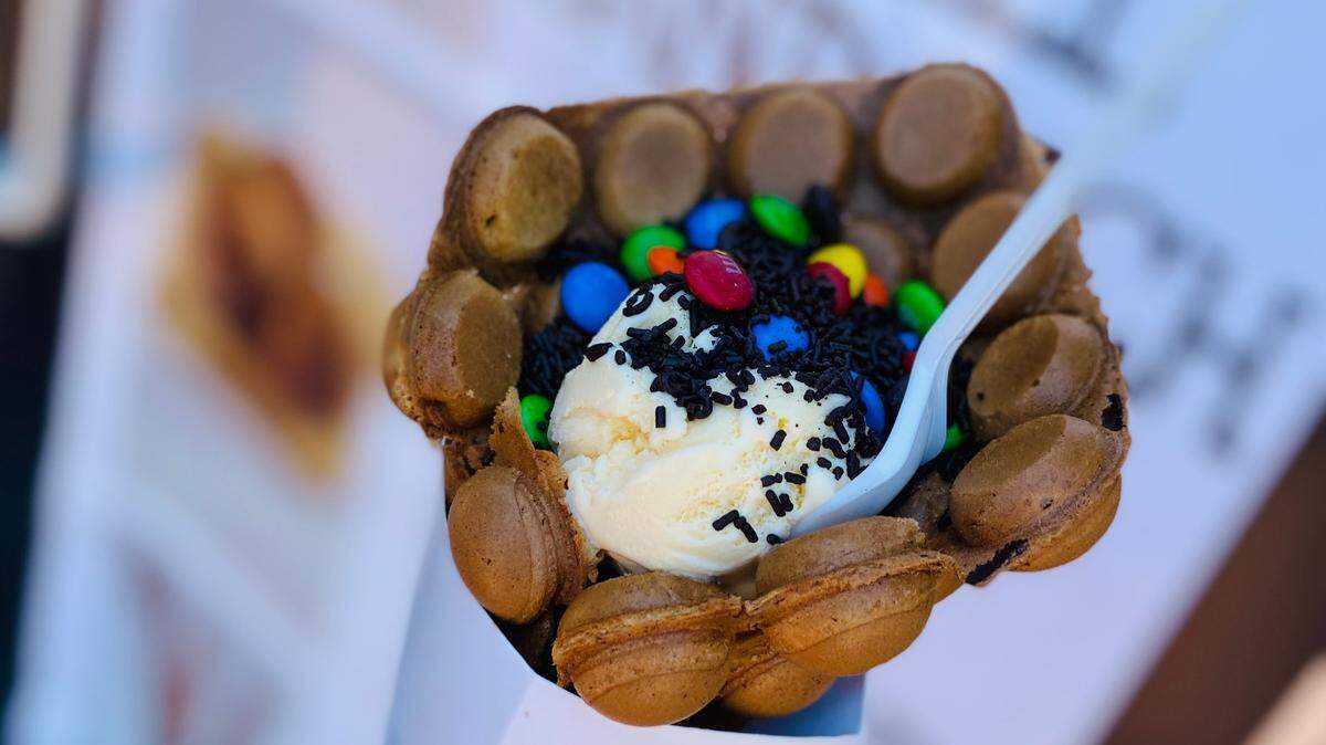 A chocolate bubble waffle filled with vanilla ice cream and topped with sprinkles and M&Ms.