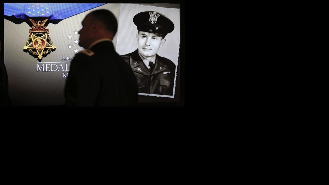 Attendees of a Hall of Heroes induction ceremony for Father Emil Kapaun at the Pentagon walk past a photo of Kapaun while entering the auditorium. Kapaun, who died in a North Korean prisoner of war camp in 1951, was posthumously awarded the Medal of Honor by President Obama the day before. (April 12, 2013)

