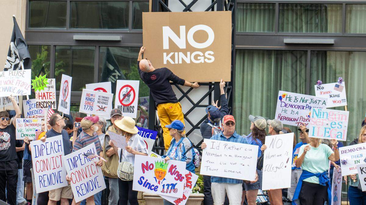 A protester at the “No Kings” demonstration hangs up a cardboard sign in downtown Wichita on Saturday, June 14, 2025.