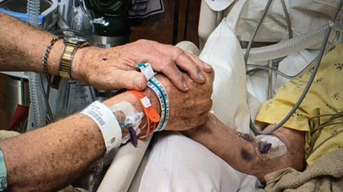 Bill McCary holds the hand of his wife, Norma McCary, in their shared room at Via Christi-St. Francis, where they were both battling COVID-19. Norma died Nov. 17. (Photo provided by the MCary family)