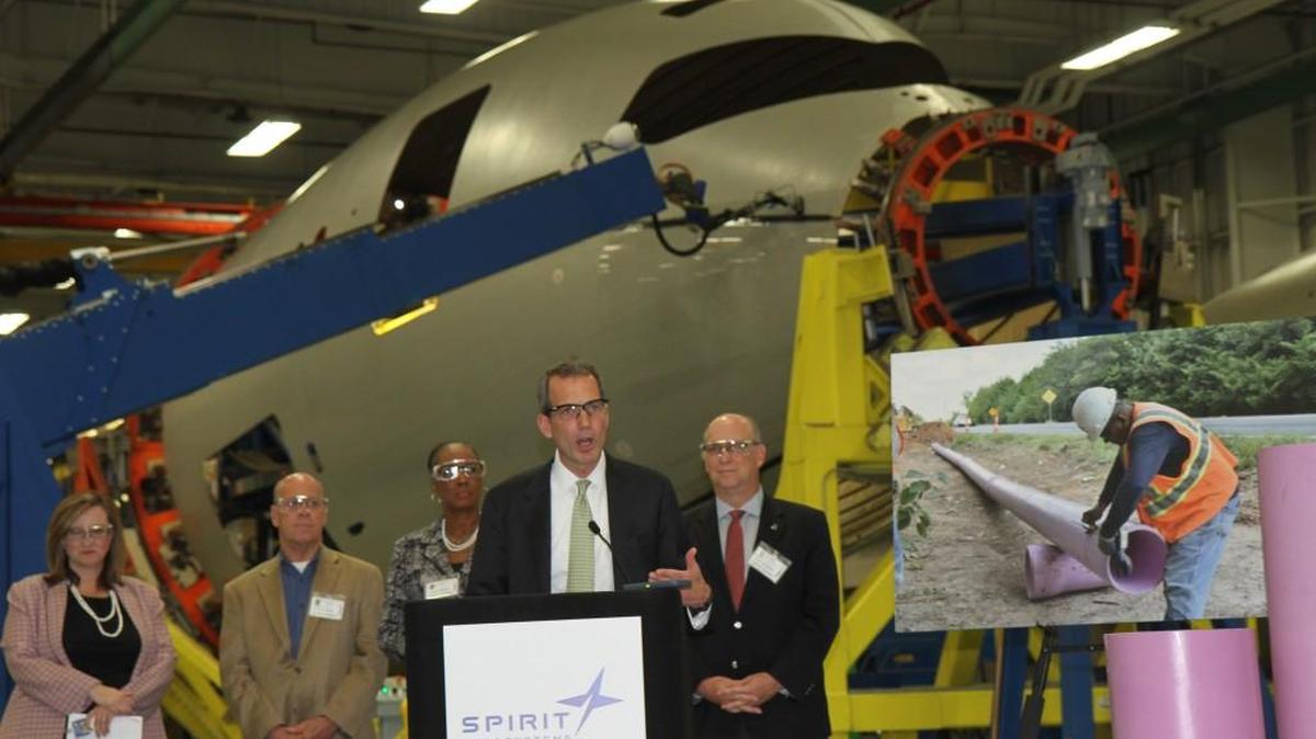 Spirit AeroSystems CEO Tom Gentile, center, speaks Monday about the company’s completion of a $4 million project to increase its use of recycled wastewater from the city for the manufacture of aircraft parts, including the Boeing 787 forward fuselage towering behind Gentile.