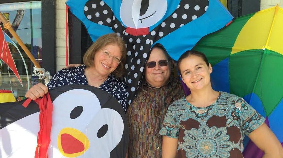
Susan Adams, left, and her husband, Mark, stand with employee Ella Rogers-Hungria and kites in front of the 750-square-foot store they’re leaving for expanded space and high ceilings near Central and Rock Road. 

