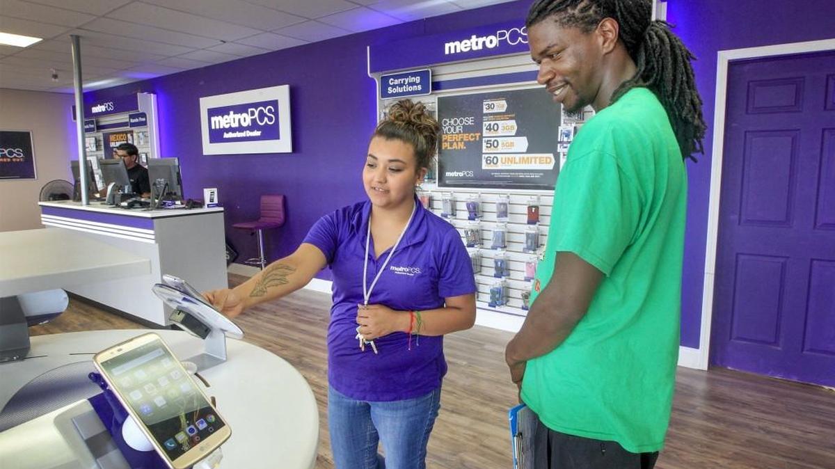 MetroPCS authorized dealer Giselle Davis, center, on Tuesday shows Jemarion Willis some of the free phones the store in College Hill Plaza is giving away with the purchase of a new plan.