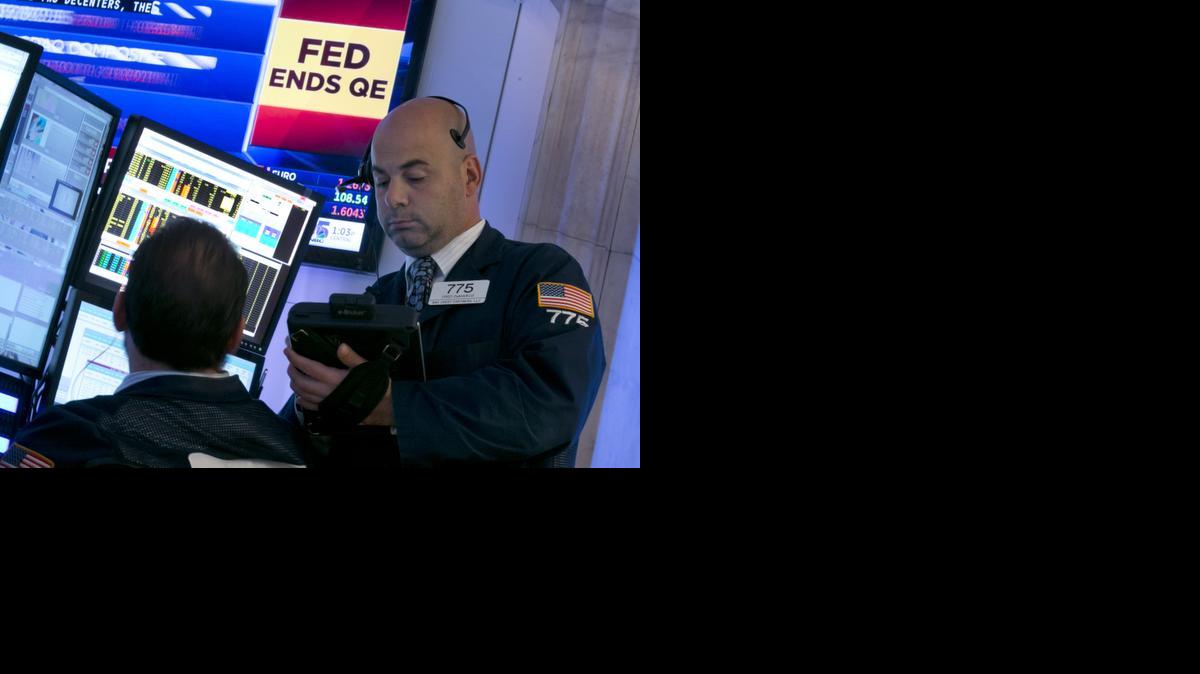 
Trader Fred DeMarco, right, works on the floor of the New York Stock Exchange Wednesday, as a television screen shows the decision of the Federal Reserve. The Fed plans to keep a key interest rate at a record low to support a U.S. job market that's improving but still isn't fully healthy and help lift inflation from unusually low levels. As expected, it's also ending a bond purchase program that was intended to keep long-term rates low. 

