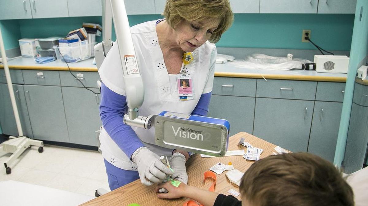 Wendy Mosiman uses a vein finder, a light that helps nurses find veins on other people, on an 8-year-old pediatric patient. Mosiman pioneered a new way of reducing pain using compressed air when giving kids shots. (Feb. 9, 2016)