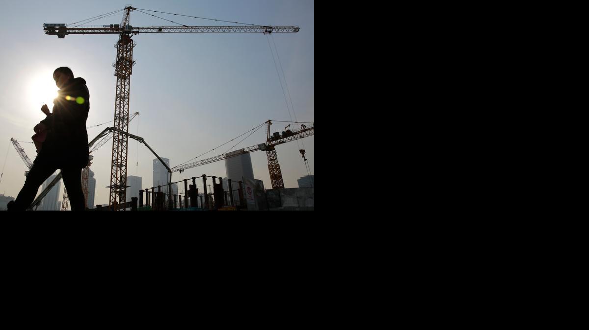 
A woman walks past a construction site at the Central Business District of Beijing, China, on Tuesday. China's economic growth slowed to 7.4 percent last year, the weakest expansion in more than two decades. 

