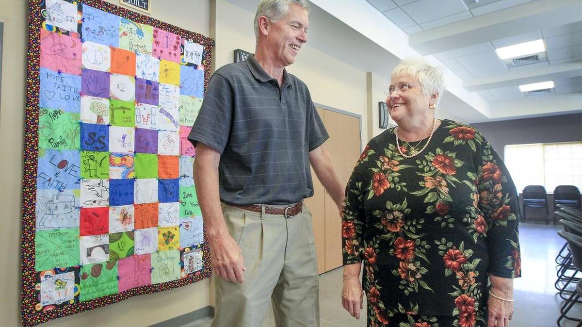 Byron Adrian, left, president of Mennonite Housing, and StepStone executive director Kit Lambertz stand by a quilt created by children of survivors of domestic violence Tuesday in the community room of the new transitional housing complex at Bluffview Place. (Sept. 6, 2016)