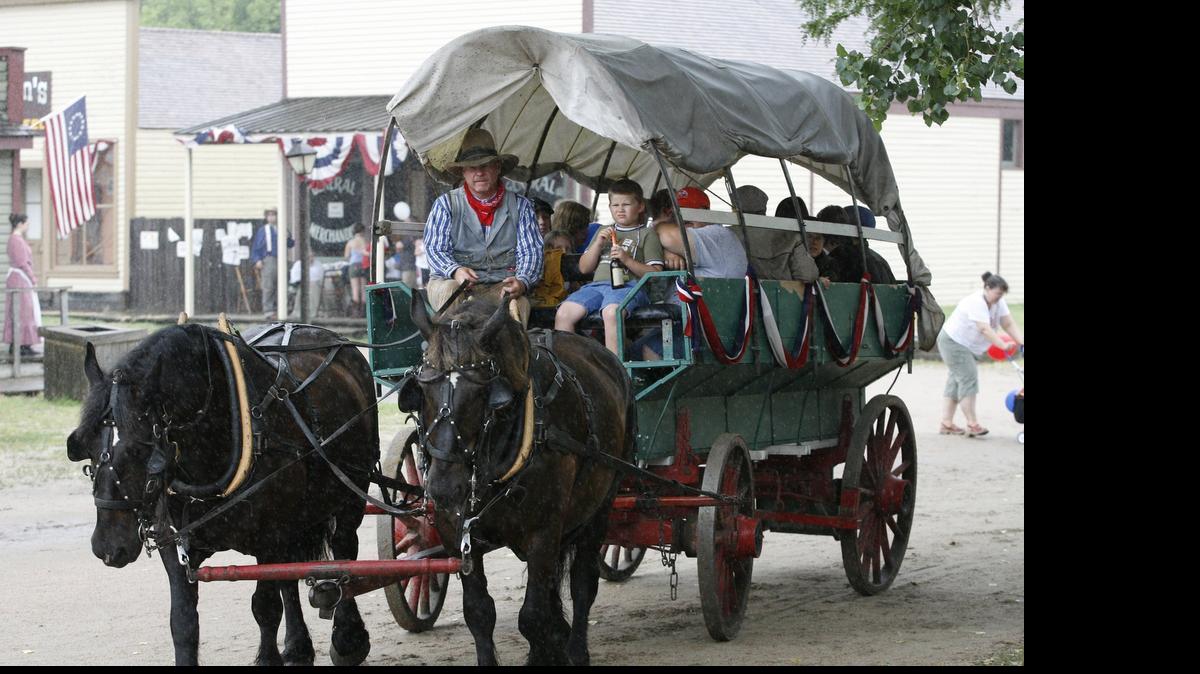 
A covered wagon drives with passengers down the streets of Cowtown.
