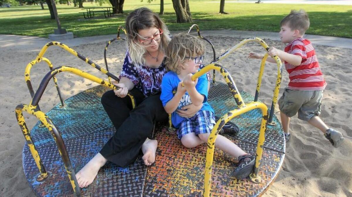 Katie Gough and her son Sully, 5, play on the merry-go-round as her other son Weston, 6, right, provides the spin Wednesday at Sycamore Park. The Gough family plans on visiting all 115 city parks this summer.