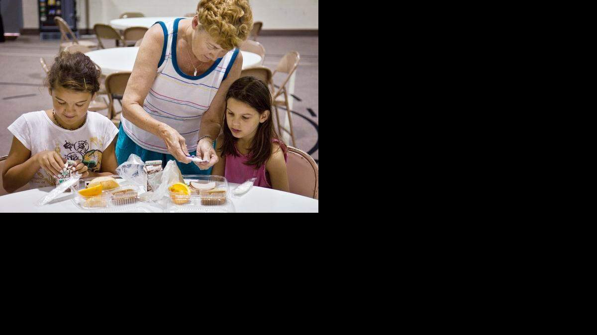
Marita Flanigan helps her granddaughters Sophia Flanigan, left, and Trinity Flanigan, with their sandwiches during the first day of the Federal Summer Meals program at West Side Christian Church in 2010. The meals for the city-wide free summer breakfast and lunch program are prepared by USD 259.
