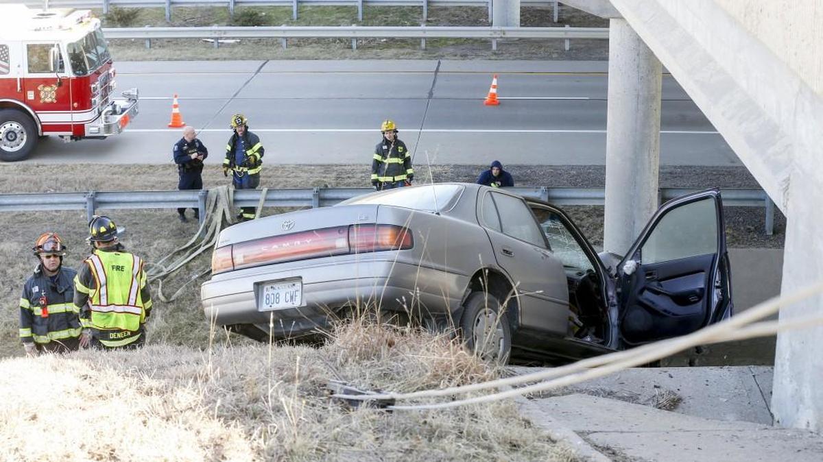 Firefighters watch as a tow truck tries to recover a car that was in an accident, where a lone driver drove off K-96 and crashed into the bridge at 13th St. around noon Wednesday. (Feb. 1, 2017)