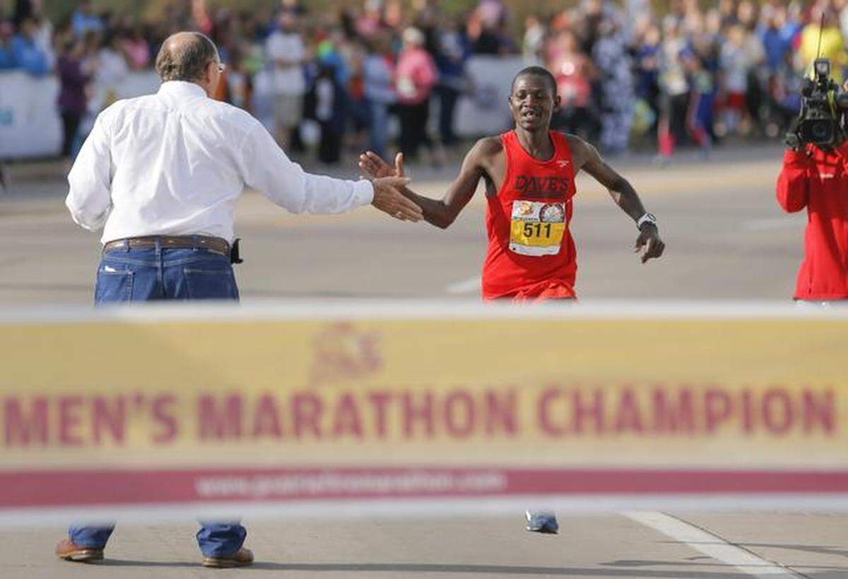 Geoffery Kiprotich gets a high-five from Bob Hanson, head of the Greater Wichita Area Sports Commision, as he comes to the finish line to win the Prairie Fire Marathon on Sunday.