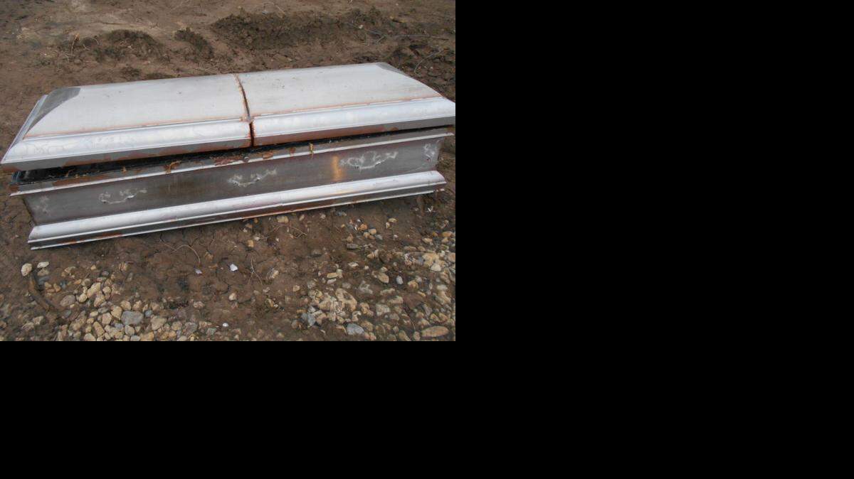 
In the photo, the handles on the side of the metal casket have been removed, and the lid has been pried open.
