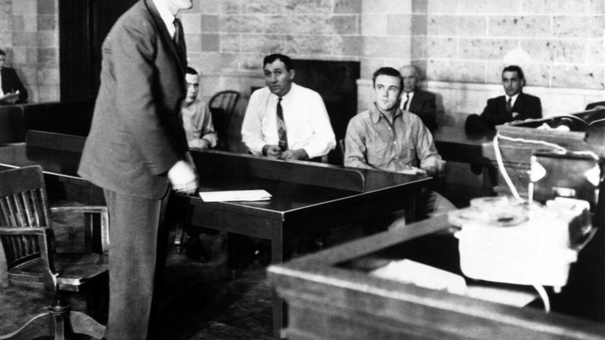 Finney County Attorney Duane West, standing left, speaks during a 1960 hearing of murder defendantds Richard Hickock, seated right, and Perry Smith, in Garden City.