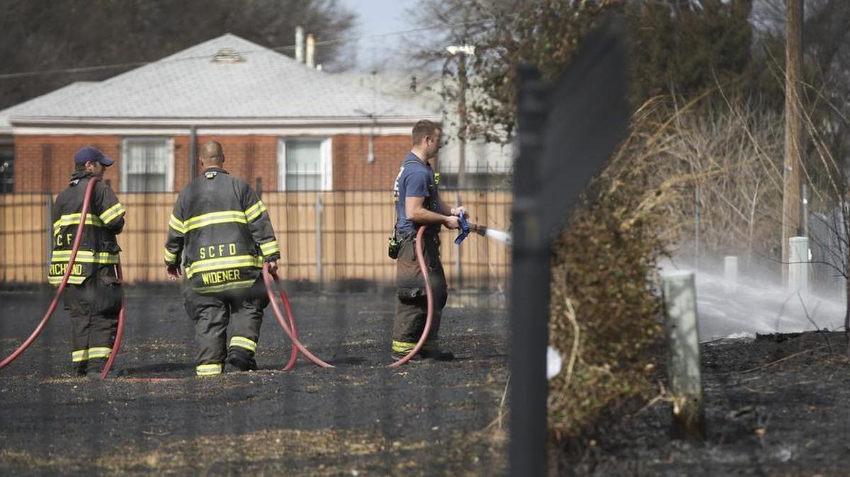 A Wichita firefighter hoses down hot spots from a grass fire near 25th and Poplar on Wednesday afternoon. The fire swept north from 25th to 26th streets, igniting a house and setting other small fires.