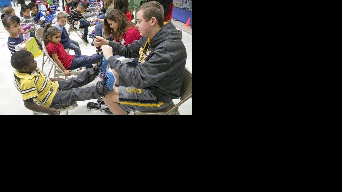 
Volunteer Zane Allen ties a new pair of shoes onto Colvin kindergartener Marcus McDowell. Colvin students received new shoes, socks, hats and gloves courtesy of Boeing, Payless Shoes, Hatman Jack’s, Papa John’s Pizza and others. (Dec. 10, 2014)
