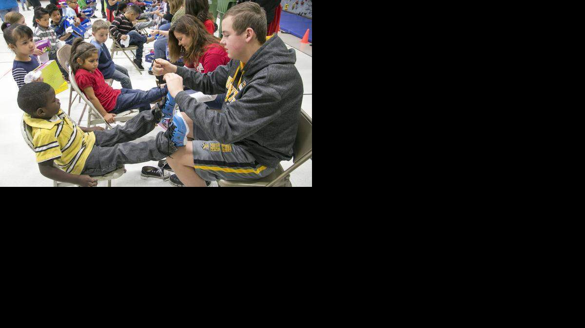 
Volunteer Zane Allen ties a new pair of shoes onto Colvin kindergartener Marcus McDowell. Colvin students received new shoes, socks, hats and gloves courtesy of Boeing, Payless Shoes, Hatman Jack’s, Papa John’s Pizza and others. (Dec. 10, 2014)
