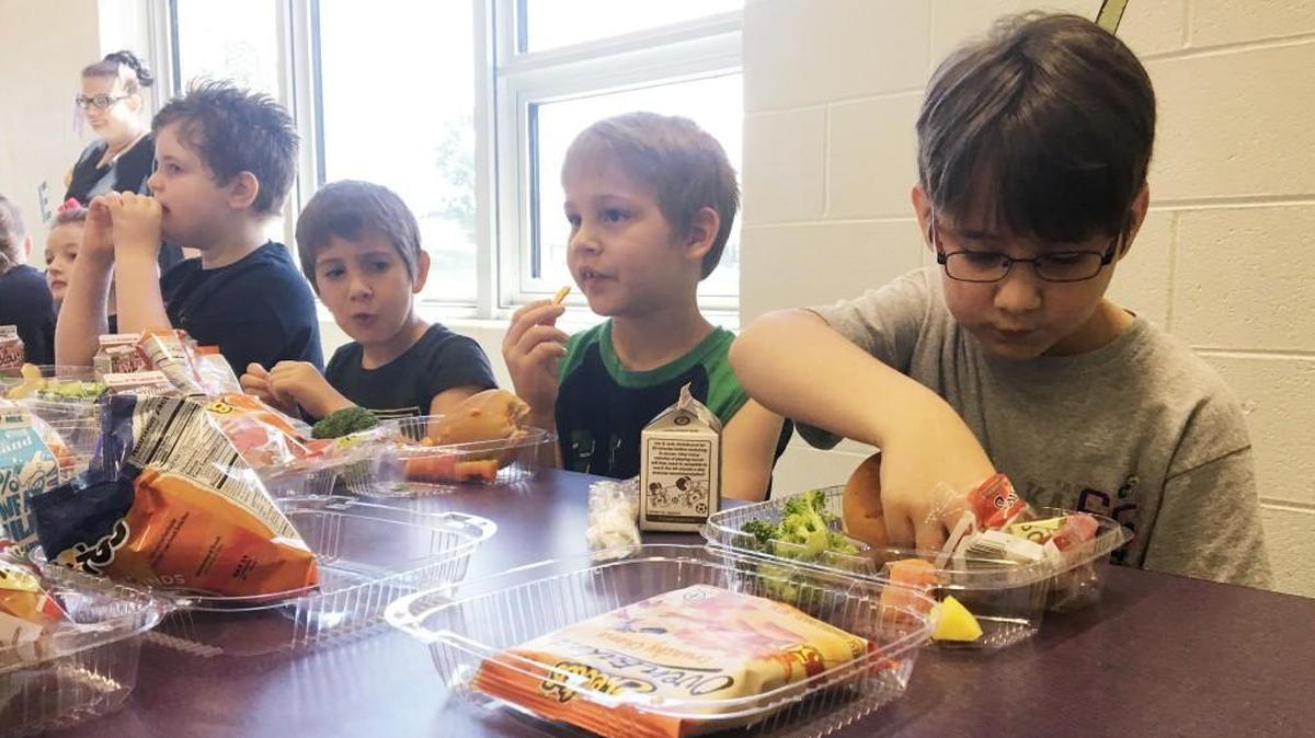 Three of Stormie Shane’s four children – from right, Hagen, 8, Kyran, 6, and Karrington, 5 – enjoy a free lunch at Linwood Elementary School on Tuesday. The district marked the launch of its free summer meals program with costumed characters and samples of tropical fruits.