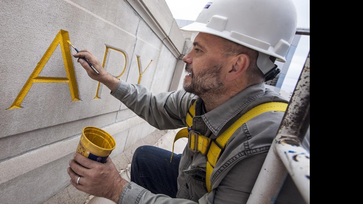 
Robert Elliot, owner of Art Effects LLC, prepares the letters above the entrance of the historic Wichita Carnegie Library for gold leaf. The sizing is a base coat to fill the porous limestone so that it will accept the thin layer of gold leaf, which, he said, “will reflect very well and will last for years.” (May 13, 2015)
