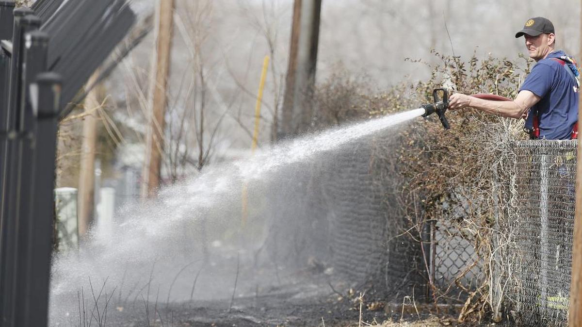 A Wichita firefighter hoses down hot spots from a grass fire near 25th and Poplar Wednesday afternoon. (March 2, 2016)