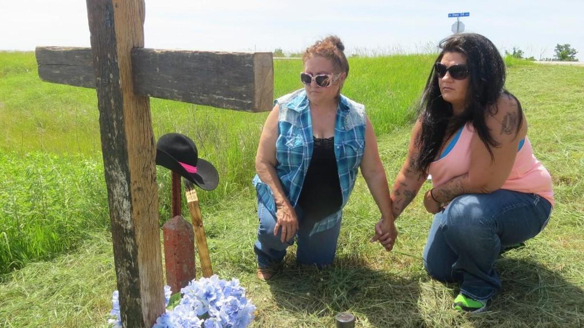 Butch Moore’s sister Mary Thomison, left, and daughter Chasity Scott kneel at a cross. It has Moore’s name carved into it. The cross sits along U.S. 54 near where a sheriff’s lieutenant fatally shot Moore. A prosecutor found that the shooting was justified, but Moore’s family has questions. (June 7, 2016)