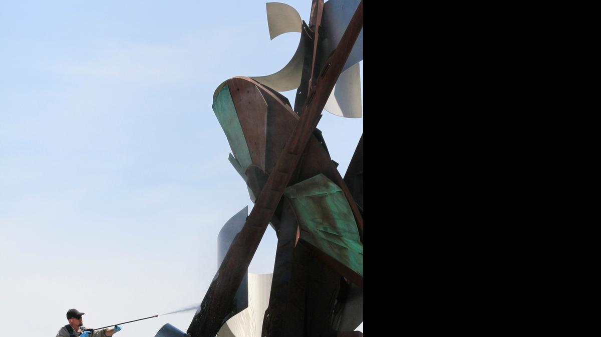 
Jason Lonergan uses a power washer to clean “Paragon,” the 38-foot, Cor-Ten steel and bronze Albert Paley sculpture in the WaterWalk area at the corner of Main and Waterman. 
