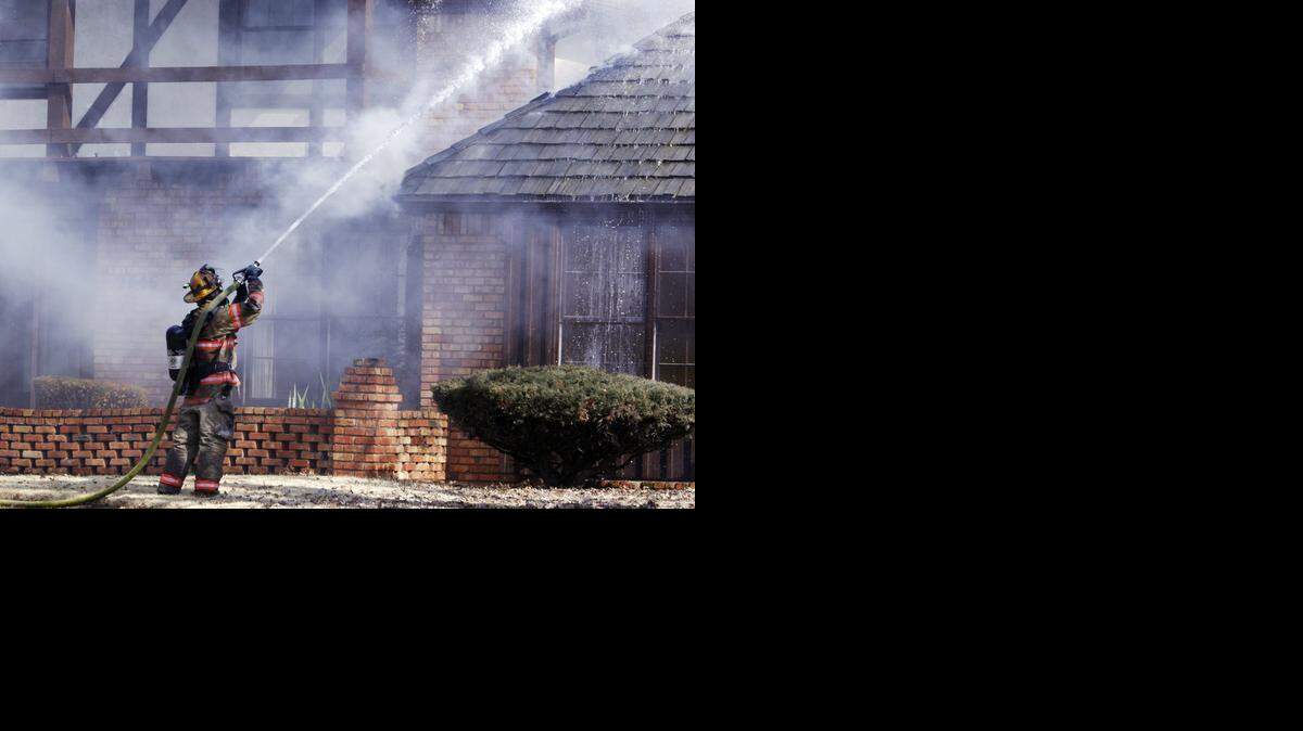
A Wichita firefighter pours water on the burning roof of a home on North Bluff in 2009 after a grass fire spread by high winds damaged several homes. 
