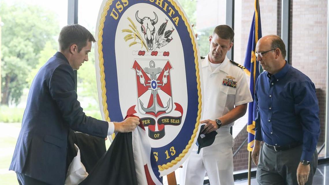 Scott Bishop, left, district director for Rep. Mike Pompeo, naval commander W. Shockey Snyder, middle, and Mayor Jeff Longwell unveil the crest of the new USS Wichita during a ceremony at the Wichita Art Museum on Saturday.