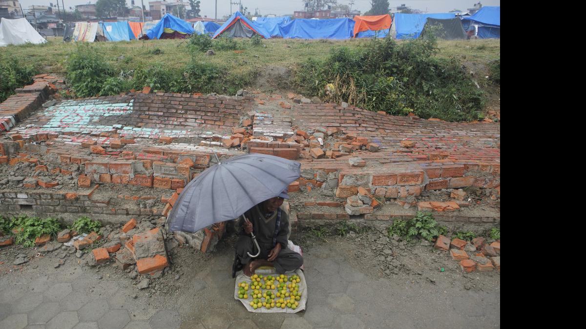 
A Nepalese street vendor waits for customers in front of a broken wall, as makeshift tents for those whose houses were damaged by the earthquake stand in the background, in Kathmandu, Nepal, Saturday, May 9, 2015. The international response has been slow to an appeal for emergency funds to help the millions of people hit by last month's earthquake in Nepal, a U.N. official said Friday. Jamie McGoldrick, the U.N.'s chief official in Nepal, said the agency had received $22 million so far against an appeal last week for $415 million to support relief efforts for the first three months in the Himalayan nation. (AP Photo/Niranjan Shrestha)
