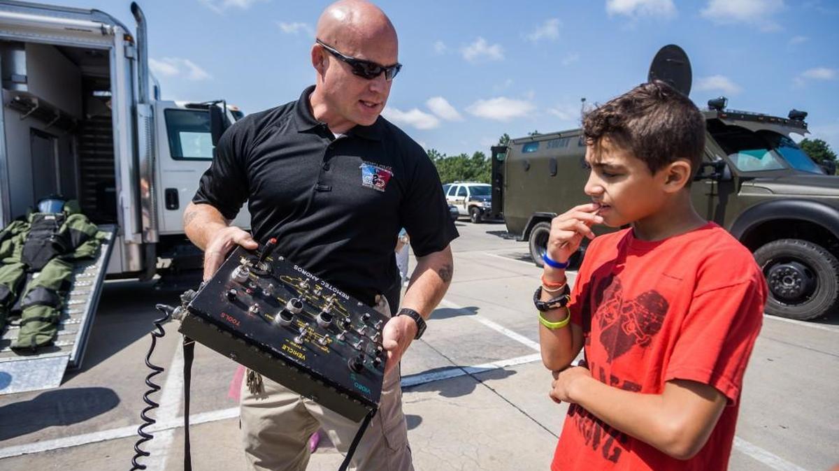 Officer John Forred, a member of the Wichita bomb squad, explains to Josiah Lemay how to use the controls for a robot detonator during a community cookout at Edgemoor Park. The cookout was hosted by Patrol East as a method to recruit more Hispanics and minorities. (Aug. 20, 2016)