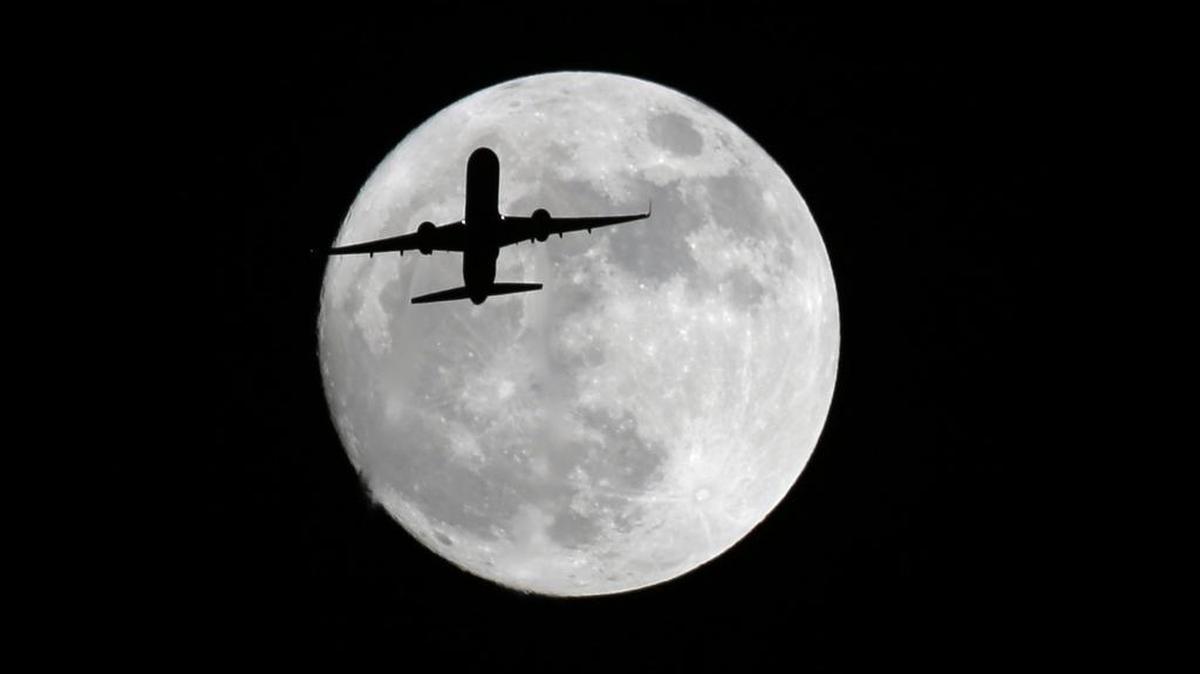 An American Airlines passenger plane passes in front of the moon, as seen from Whittier, Calif., Sunday, Nov. 13, 2016. The “flower moon” will peak in early May this weekend and be visible from southwestern Illinois. (AP Photo/Nick Ut)