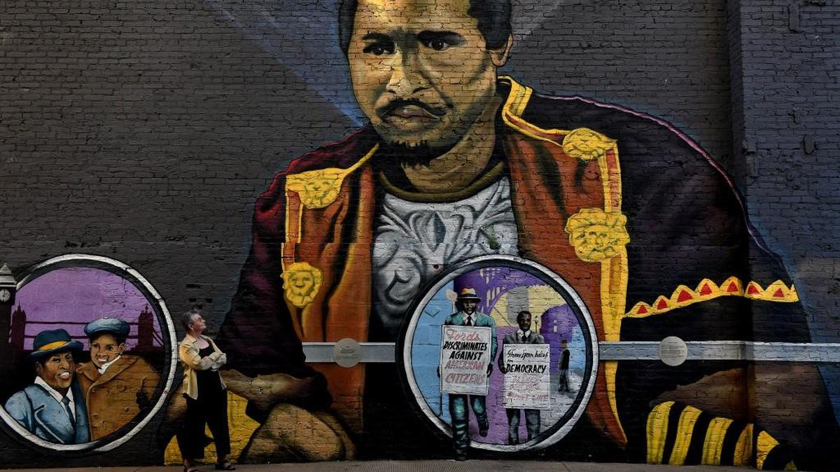 Perry Frank, who has delved into the District of Columbia murals for two decades, stands beside the interactive mural of Paul Robeson in an alley.