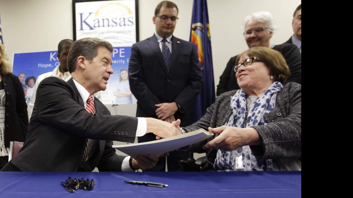 
Gov. Sam Brownback, left, shakes hands with Department for Children and Families secretary Phyllis Gilmore, right, after signing a welfare reform bill into law in Topeka on Thursday. 
