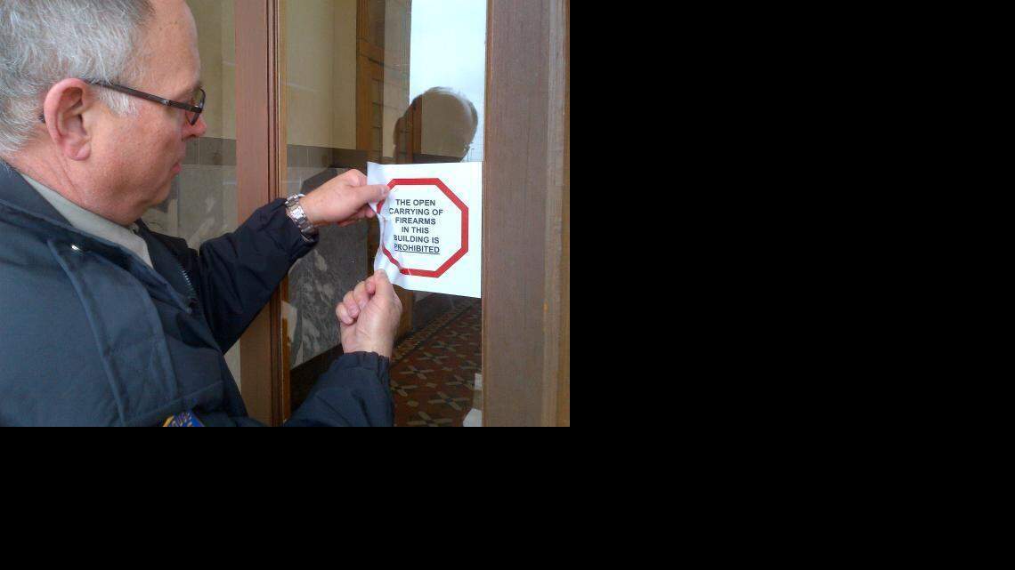 
Darrell Haynes, chief of Sedgwick County Courthouse police, removes a “no open carry” sign from the Historic Courthouse door. (March 24, 2015)
