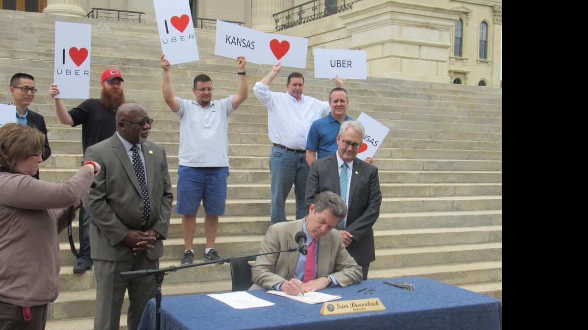 
Gov. Sam Brownback is joined by Rep. Willie Dove, R-Bonner Springs, left, Sen. Tom Hawk, D-Manhattan, and a fleet of Uber drivers as he signs a bill designed to bring the ride-hailing service back to Kansas on Friday. 
