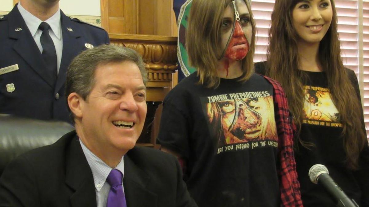 
Gov. Sam Brownback is joined by Faith Tucking, 15, and her aunt, Devan, as he promotes "Zombie Preparedness Month." 

