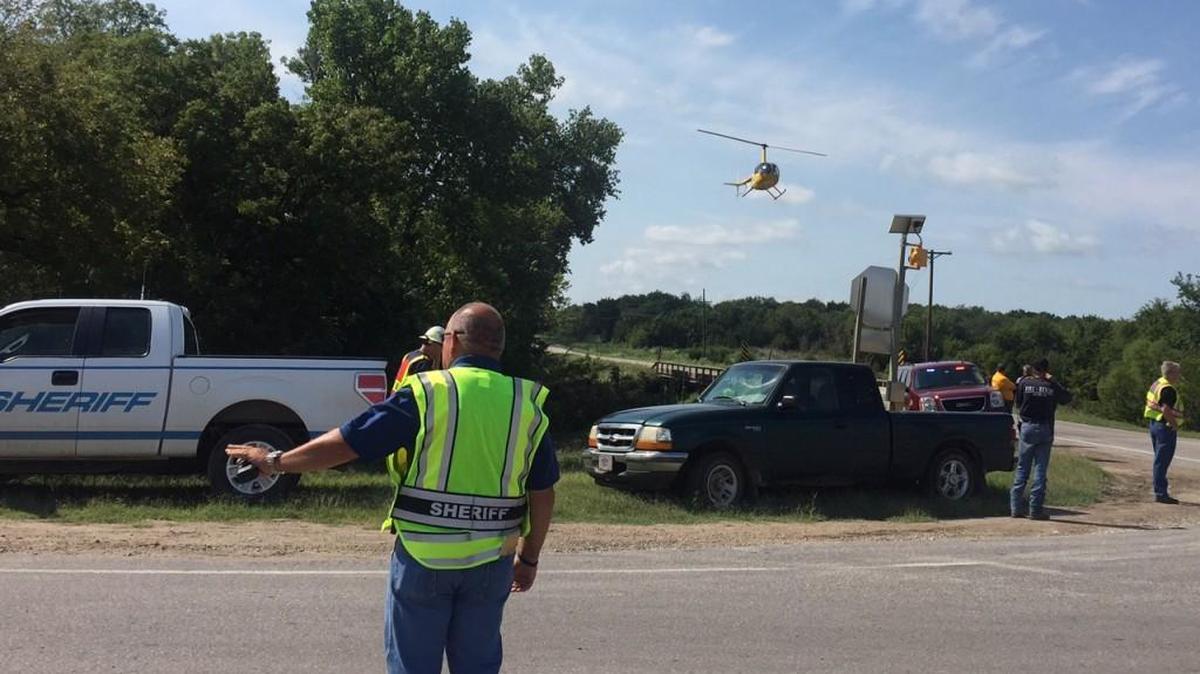A helicopter searching for a Wichita man missing in a flash flood comes in for a landing as Butler County Sheriff Kelly Herzet, foreground, stops traffic on Southwest 210th Road south of Rose Hill.