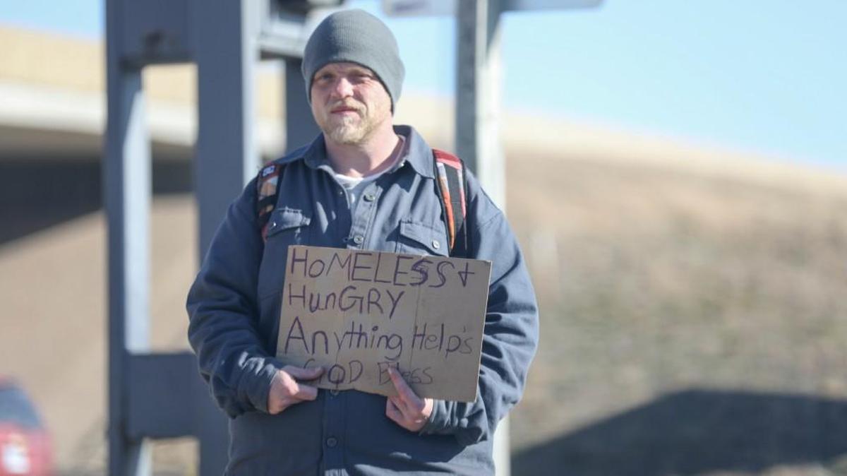 A man stands by the intersection of K-96 and Rock road holding a sign as cars drive by Tuesday.