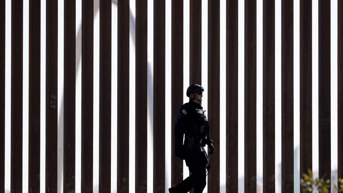 A U.S. Customs and Border Protection Special Response Team officer walks along a border wall, as the Monumental Arch in Tijuana, Mexico, sits behind, Sunday, Nov. 25, 2018, in San Diego. (AP Photo/Gregory Bull)
