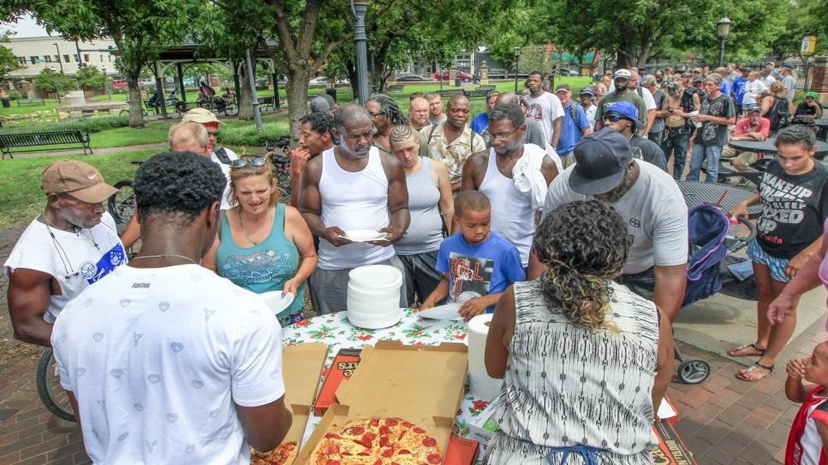 Members of the Victory House Ministry hand out free pizza to the homeless at Naftzger Park last month.