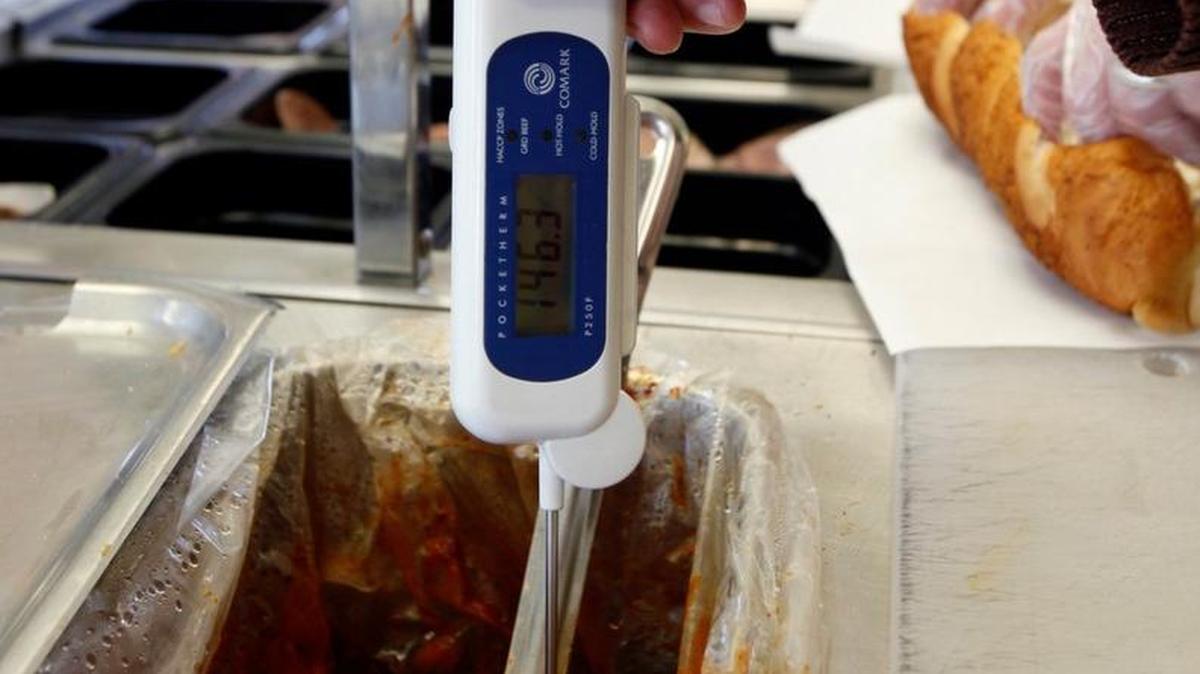 A Public Health Sanitation worker prods a meatball with a thermometer to see whether it is the correct temperature during a restaurant inspection.