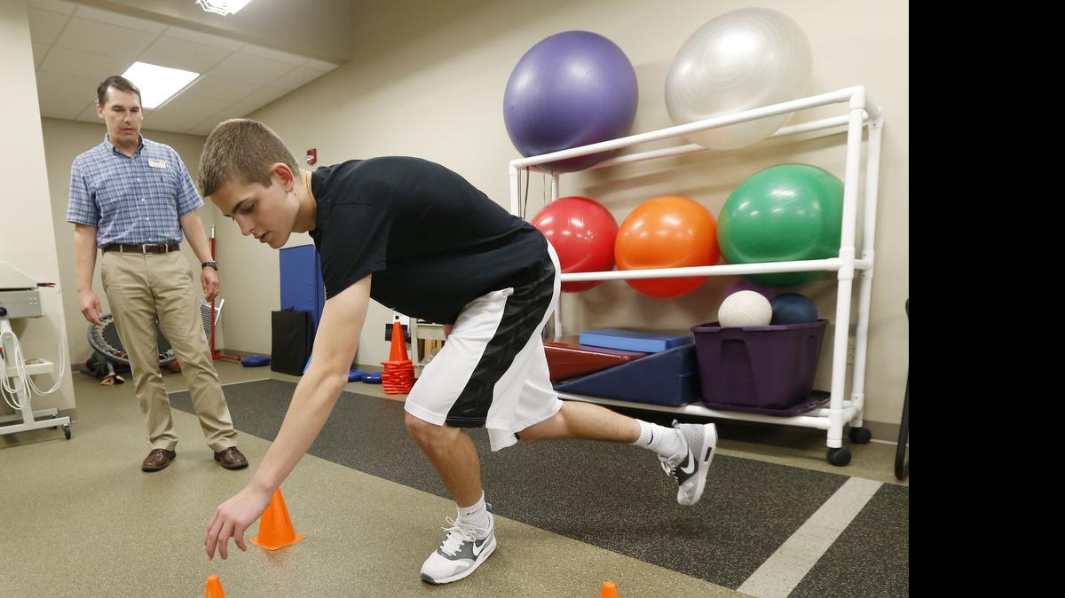 
 Hesston High grad Grant Raleigh goes through physical therapy with physical therapist Jeff Couchman at Pinnacle Rehab in Newton. Raleigh, a quarterback for Hesston, won't play in the Shrine bowl this year after being severely injured in a skiing accident in March. (July 7, 2015)
