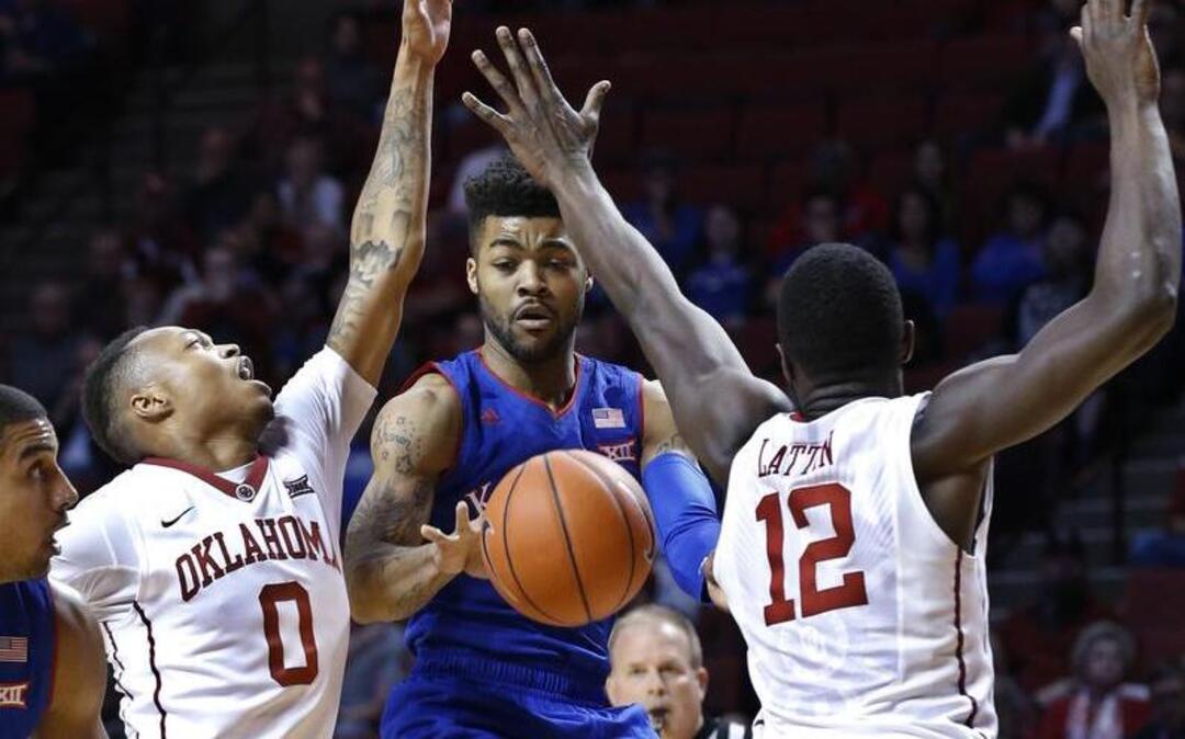 Kansas guard Frank Mason passes between Oklahoma guard Darrion Strong-Moore, left, and forward Khadeem Lattin during the first half Tuesday in Norman, Okla.